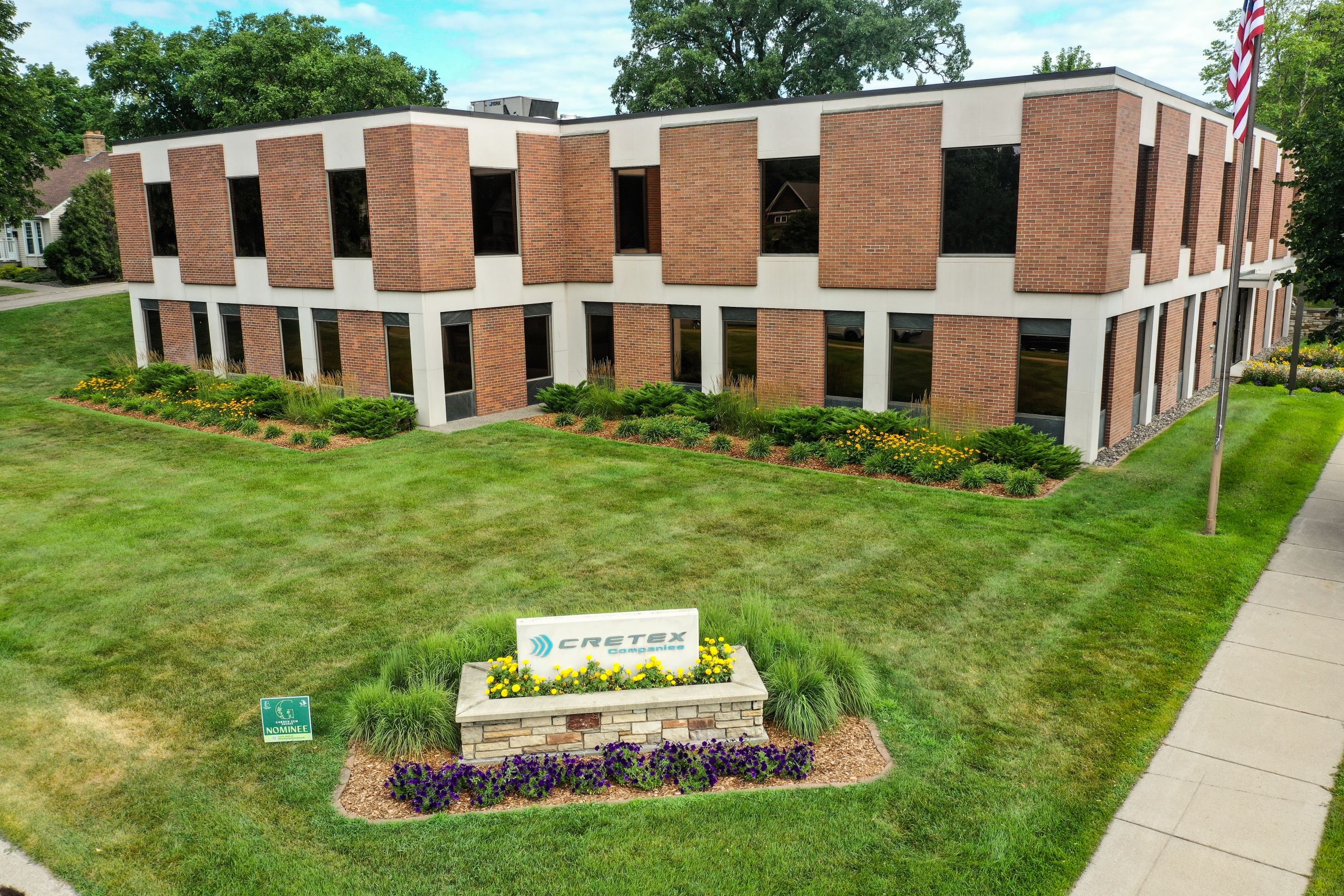 outside of a commercial building with green grass and plants arranged around at company sign